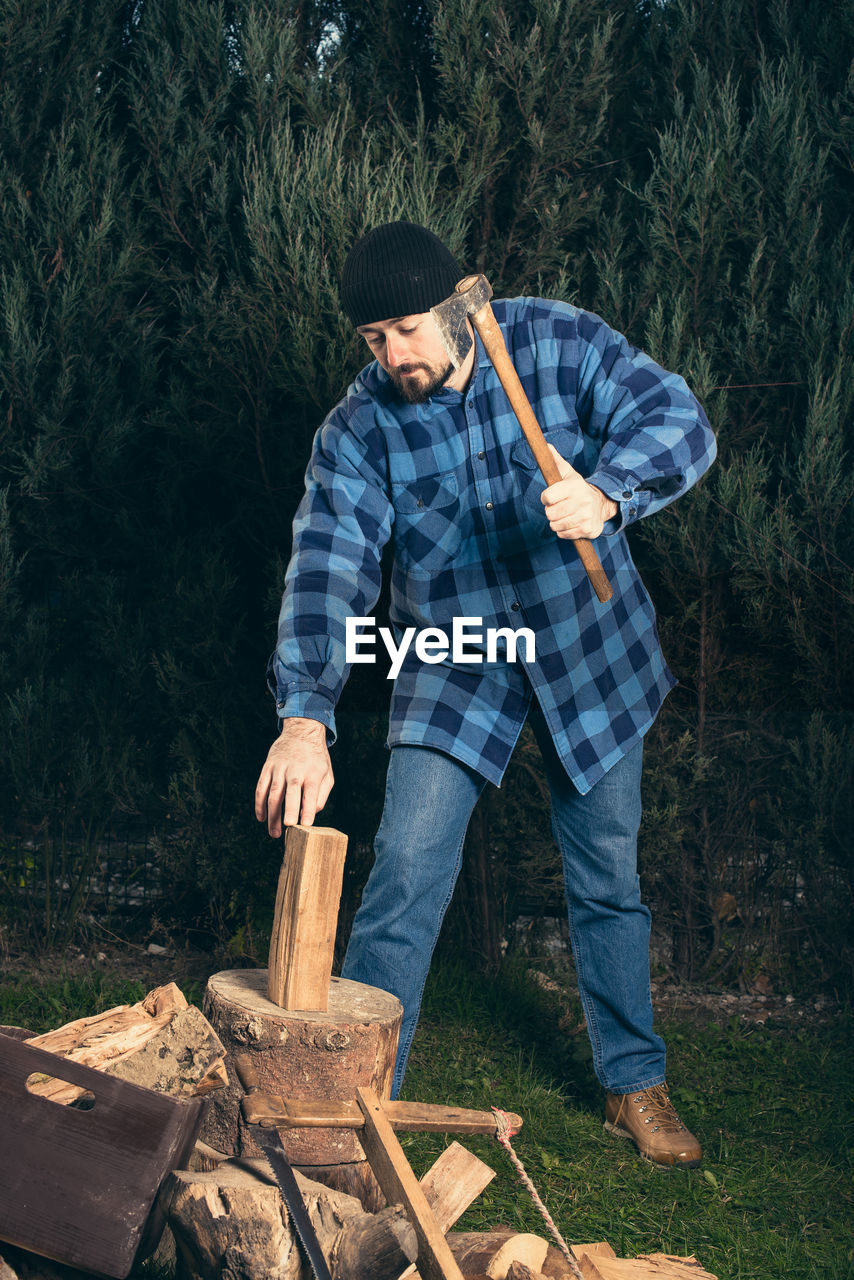 Full length of lumberjack chopping wood from axe against trees at forest