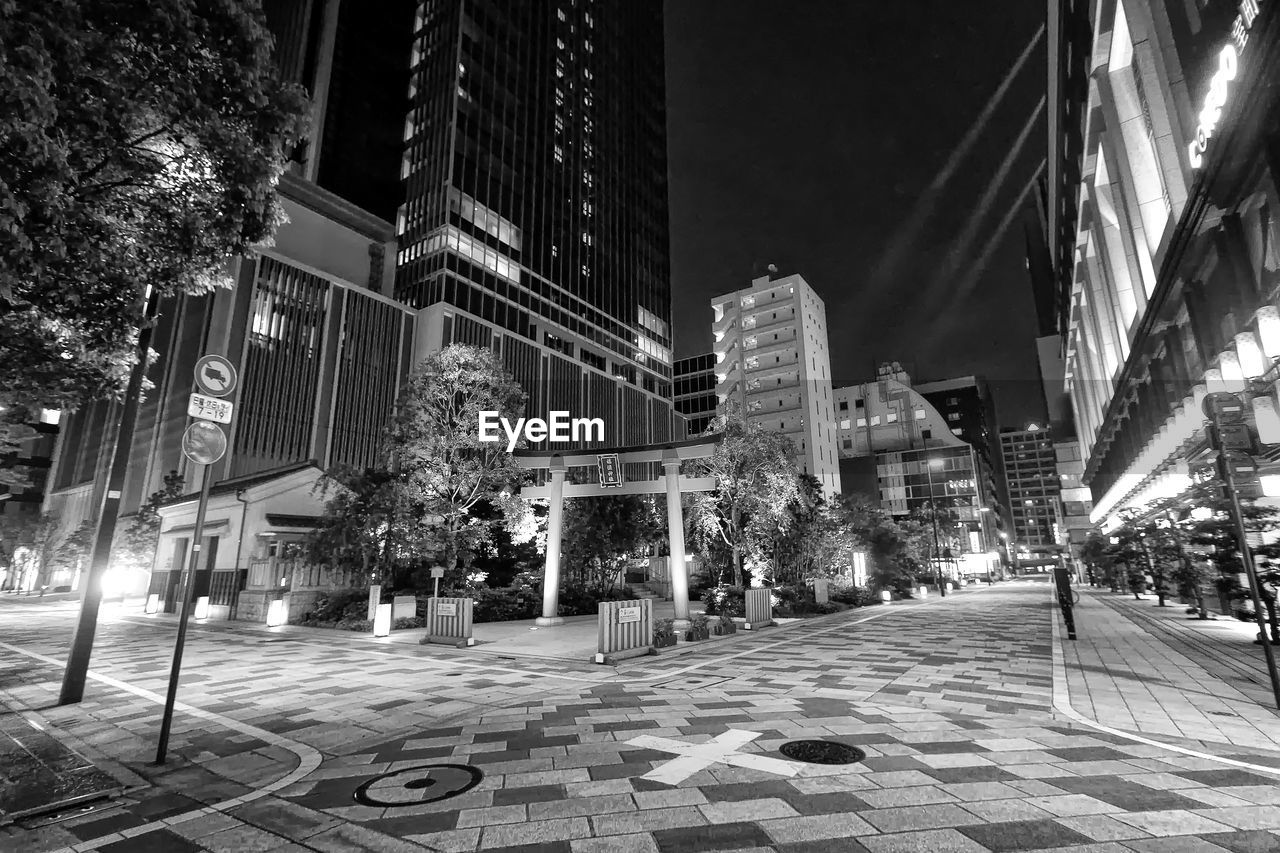 architecture, built structure, building exterior, city, street, road, black and white, urban area, night, metropolis, illuminated, cityscape, building, monochrome photography, skyscraper, monochrome, downtown, city life, city street, office building exterior, nature, travel destinations, outdoors, footpath, tree, transportation, street light, black, plant, sky, sign, infrastructure