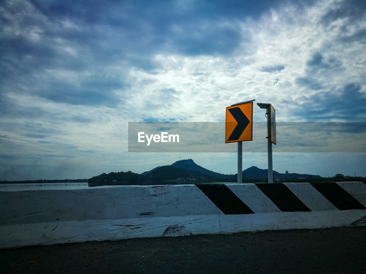 ROAD SIGN BY POLE AGAINST SKY