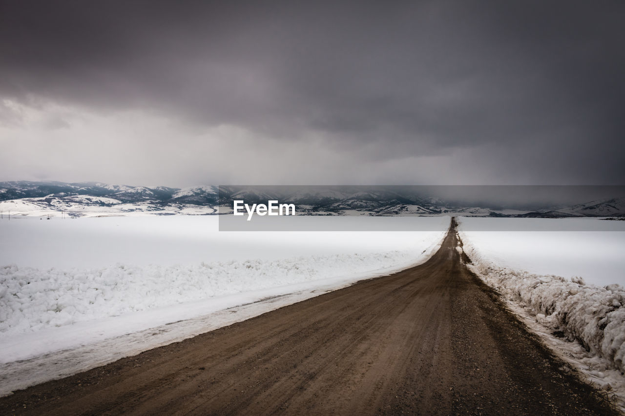 Road amidst snowcapped landscape against sky during winter