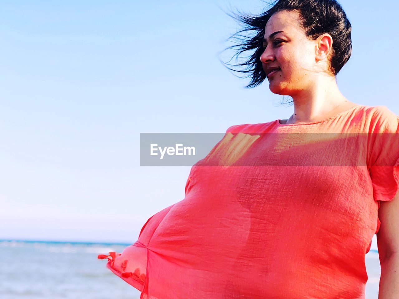 WOMAN STANDING ON BEACH AGAINST SKY