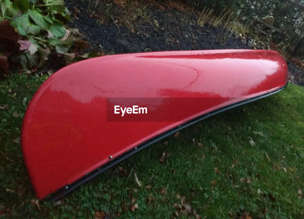 High angle view of red canoe moored upside down on grass