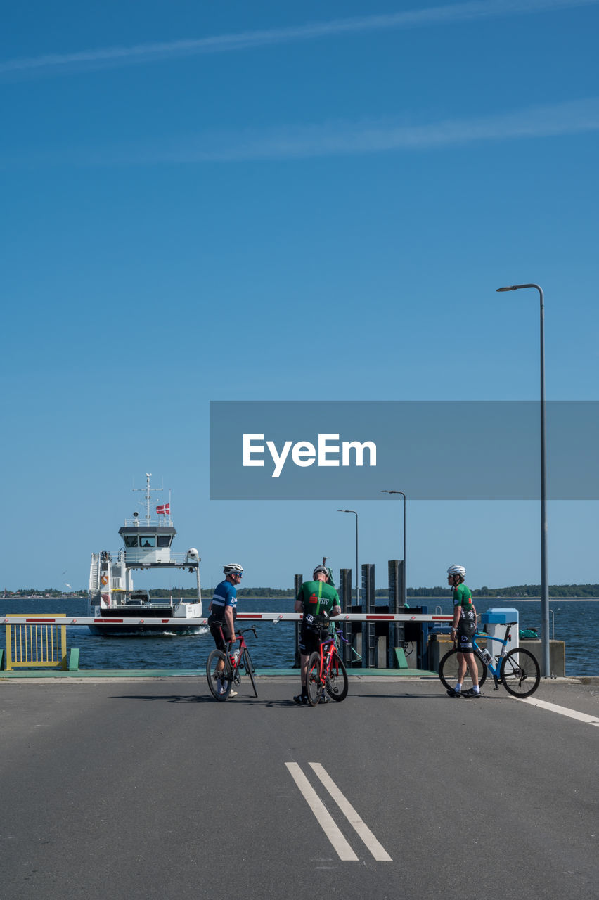transportation, sky, mode of transportation, road, bicycle, water, group of people, sea, nature, clear sky, coast, day, men, blue, city, land vehicle, vehicle, adult, sports, street, highway, travel, cycling, architecture, copy space, ship, motion, beach, boardwalk, walkway, sunny, outdoors, full length, nautical vessel, small group of people, riding, lifestyles, race track, headwear, on the move, infrastructure, sunlight, activity, motor vehicle, women, helmet, road marking