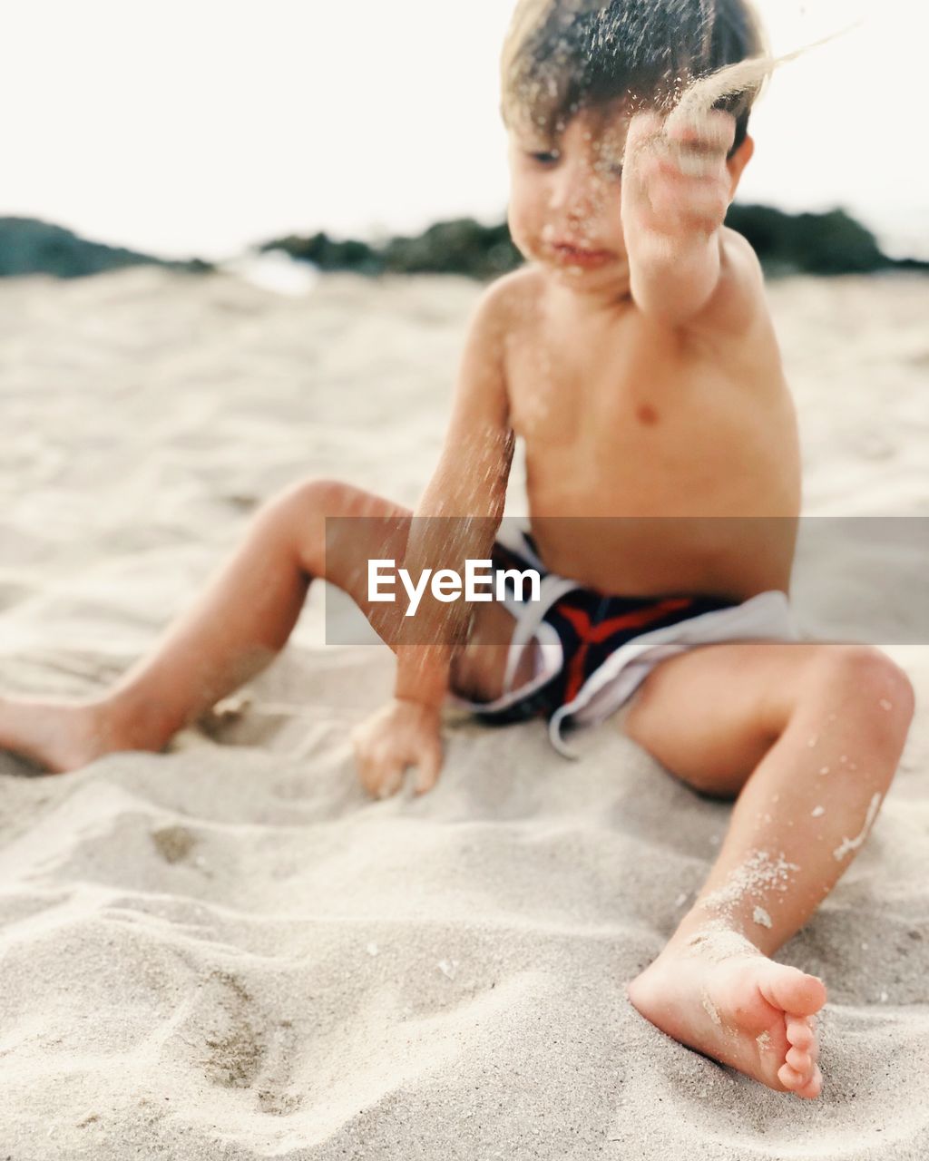 Shirtless boy spilling sand at beach