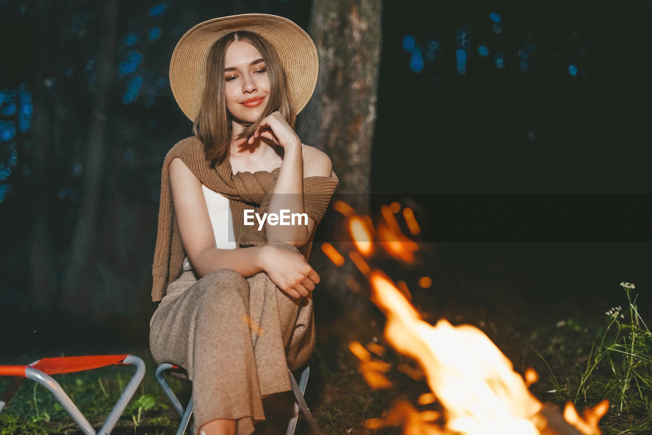 Young woman sitting in forest by campfire