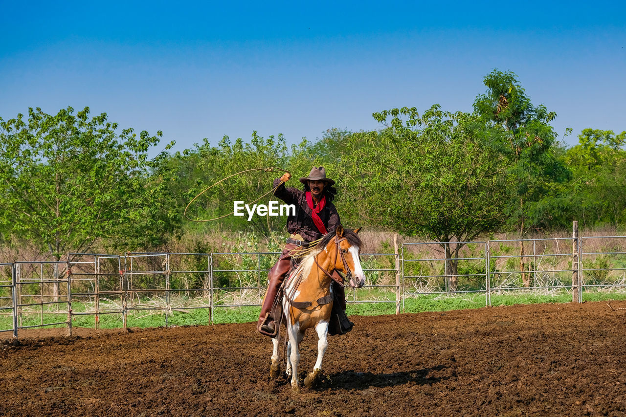 Cowboy riding horse at ranch on sunny day