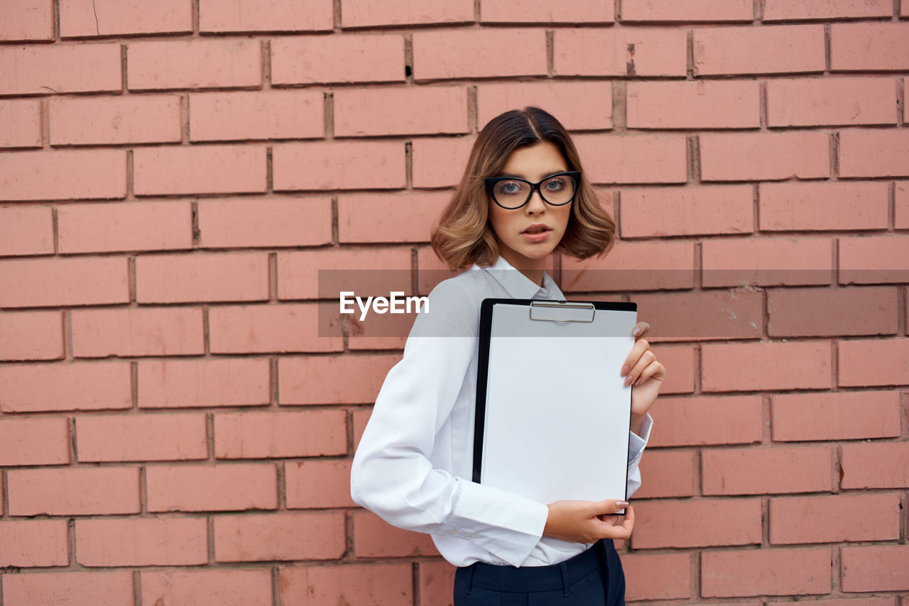 Young woman holding clipboard against wall