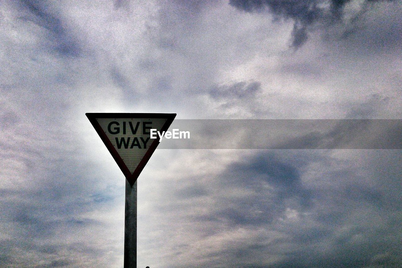 LOW ANGLE VIEW OF SIGN BOARD ON ROAD AGAINST CLOUDY SKY