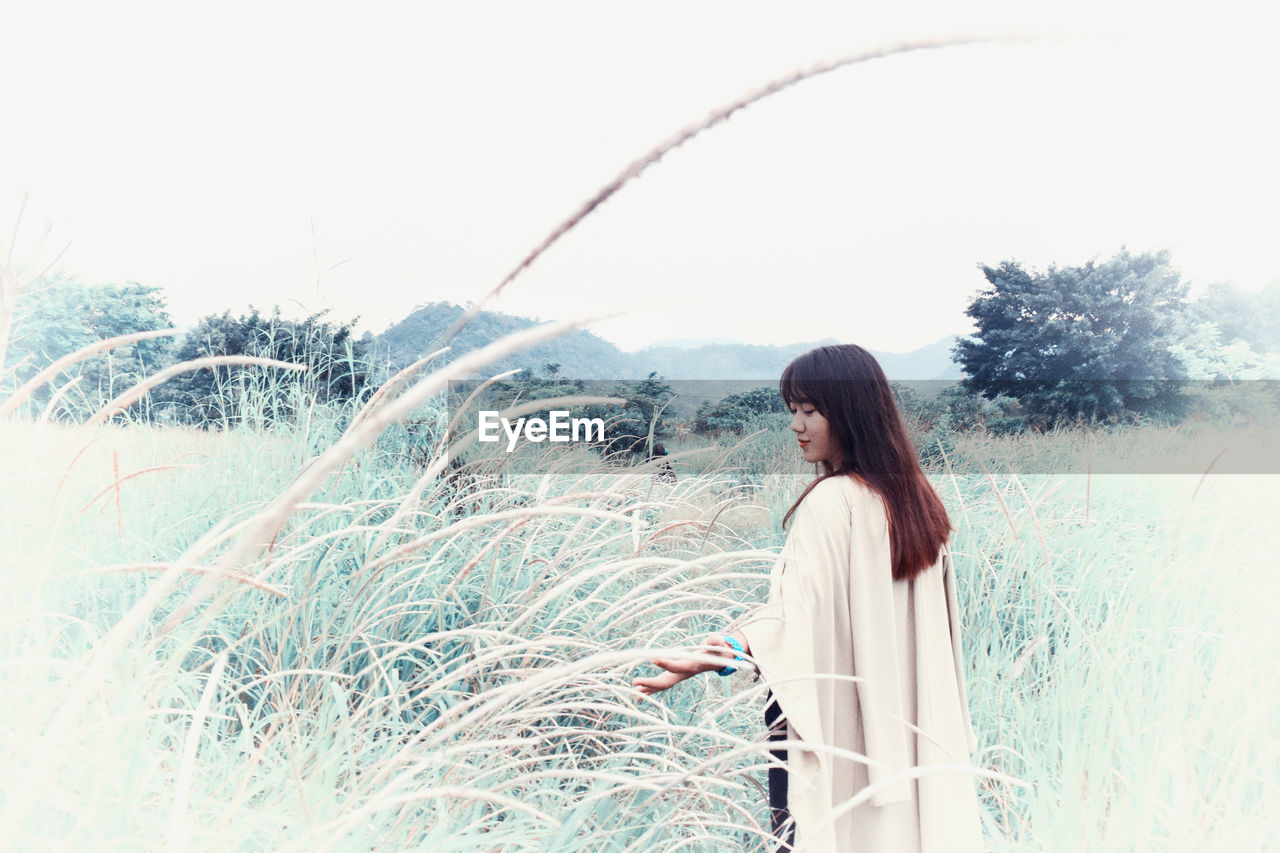 Young woman standing amidst grass on land