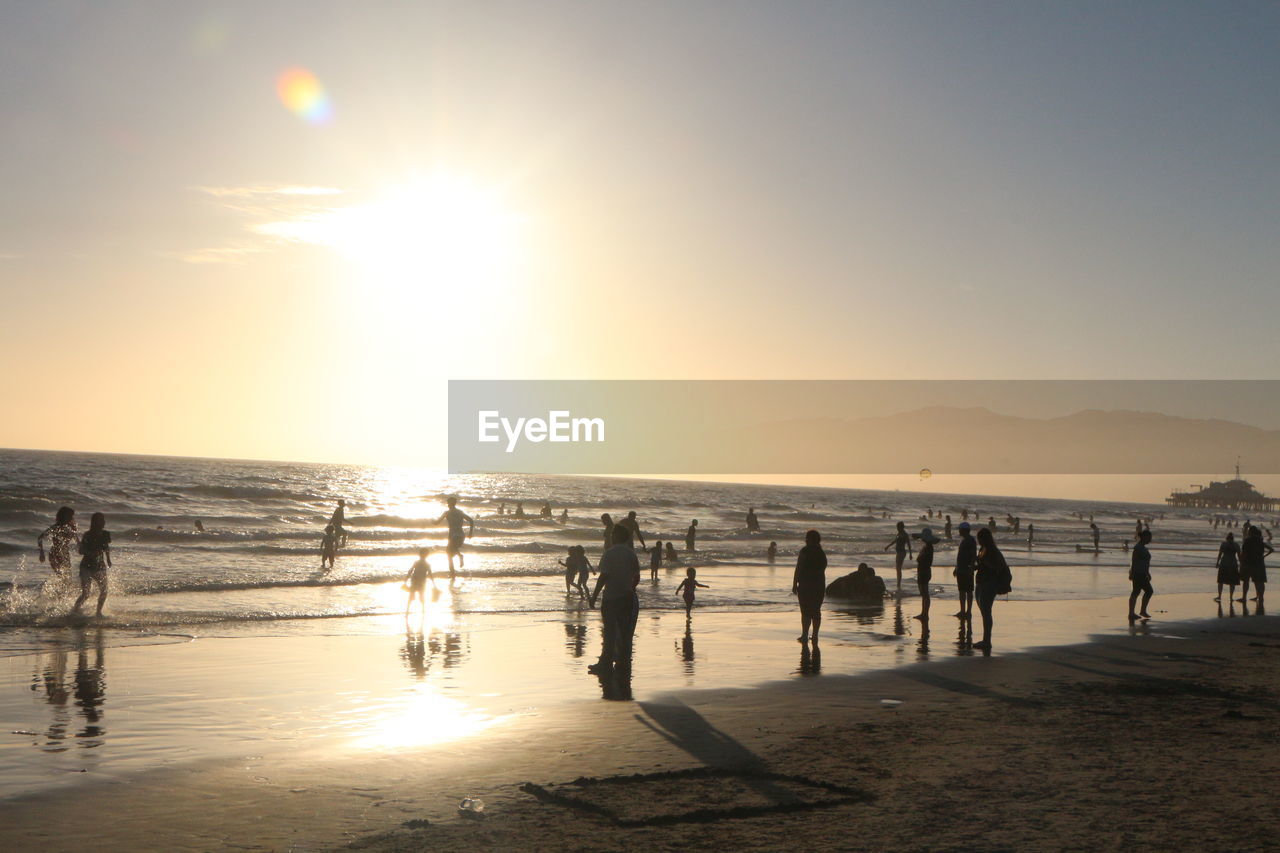 PEOPLE ON BEACH AGAINST SKY AT SUNSET