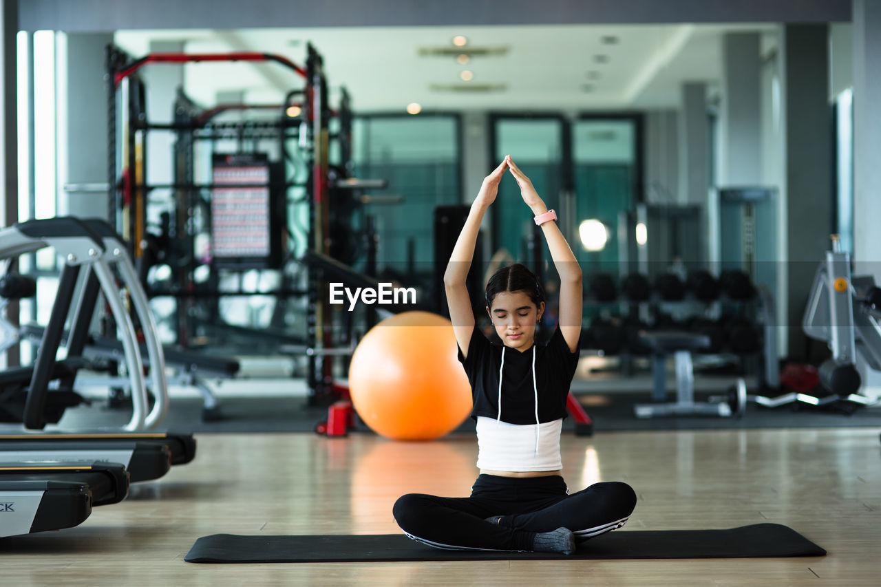 Full length of girl meditating at gym