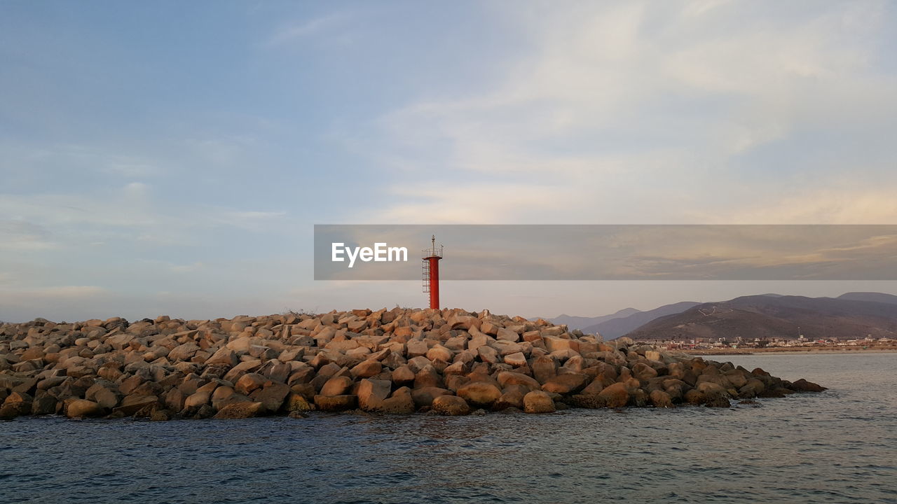 Lighthouse on rock by sea against sky