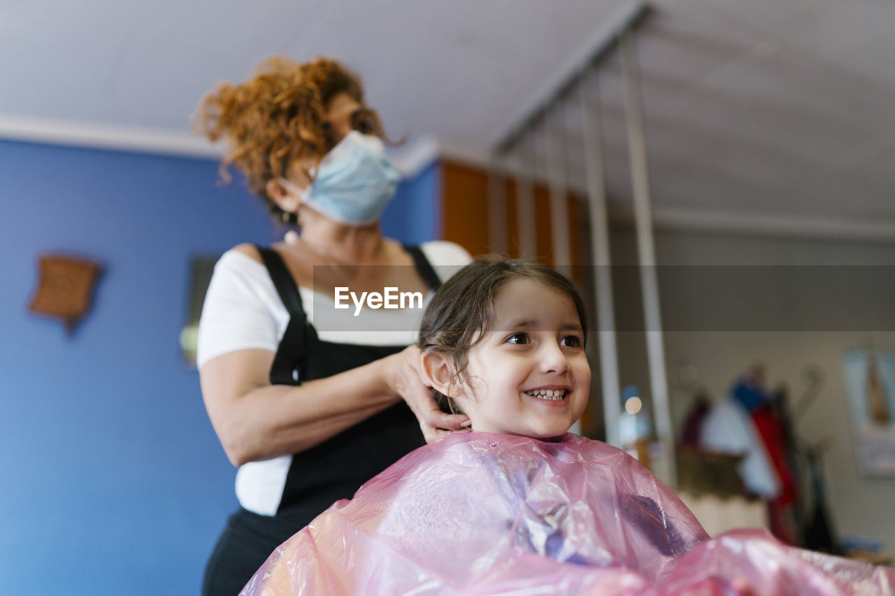 Mature female hairdresser with cute customer at hair salon during covid-19