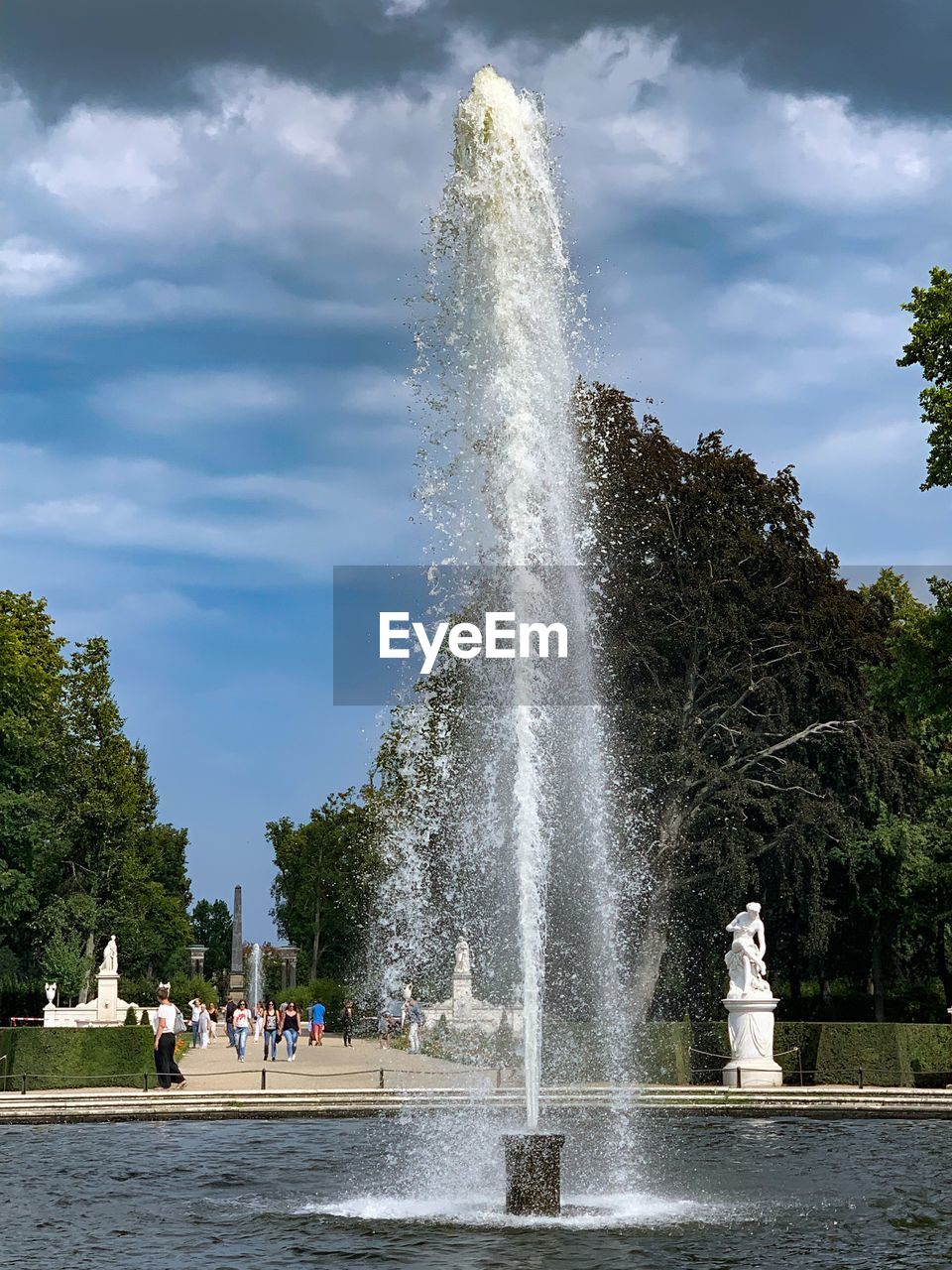 People on fountain against trees and plants against sky