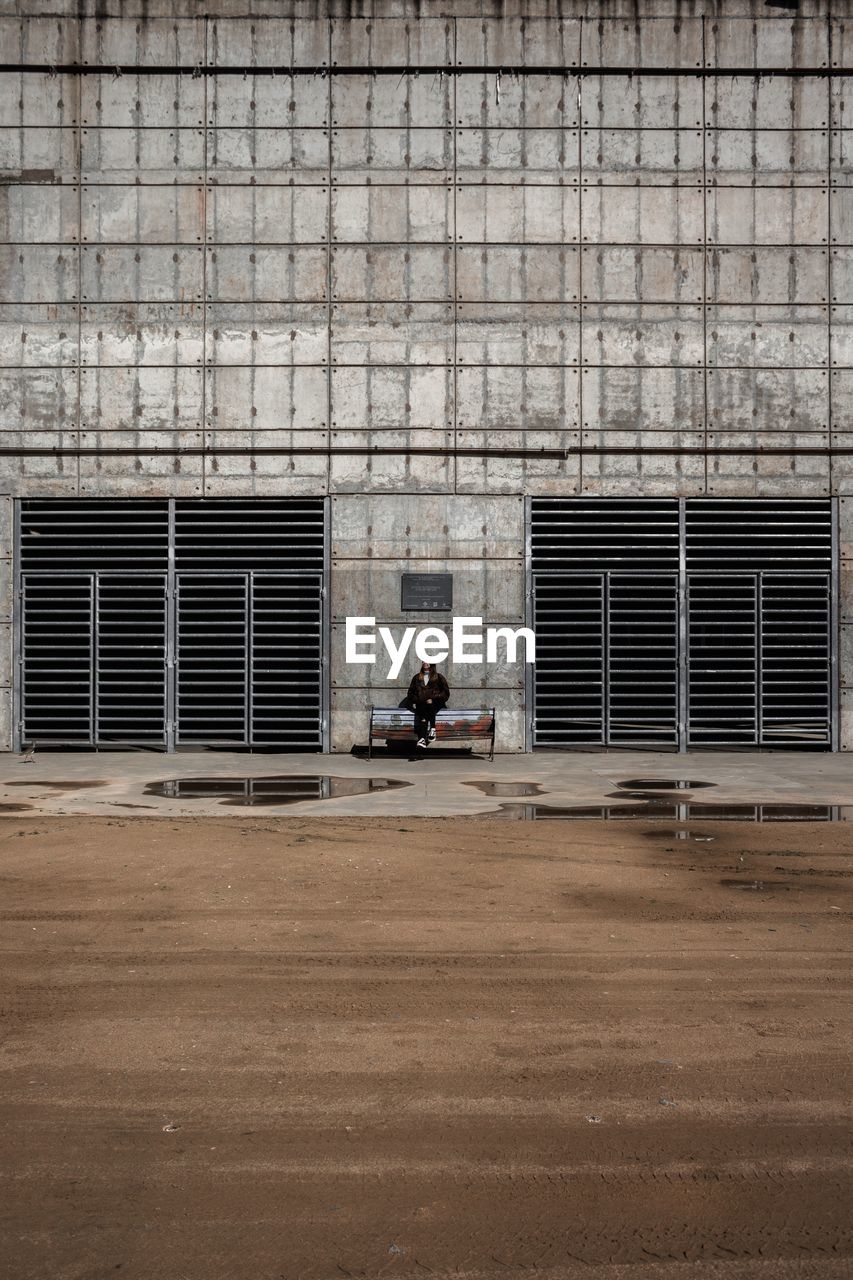 Woman sitting on bench against building