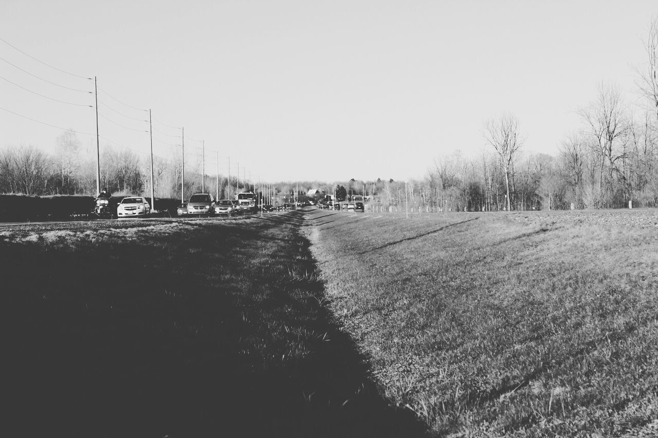 Cars on country road by grassy field against clear sky