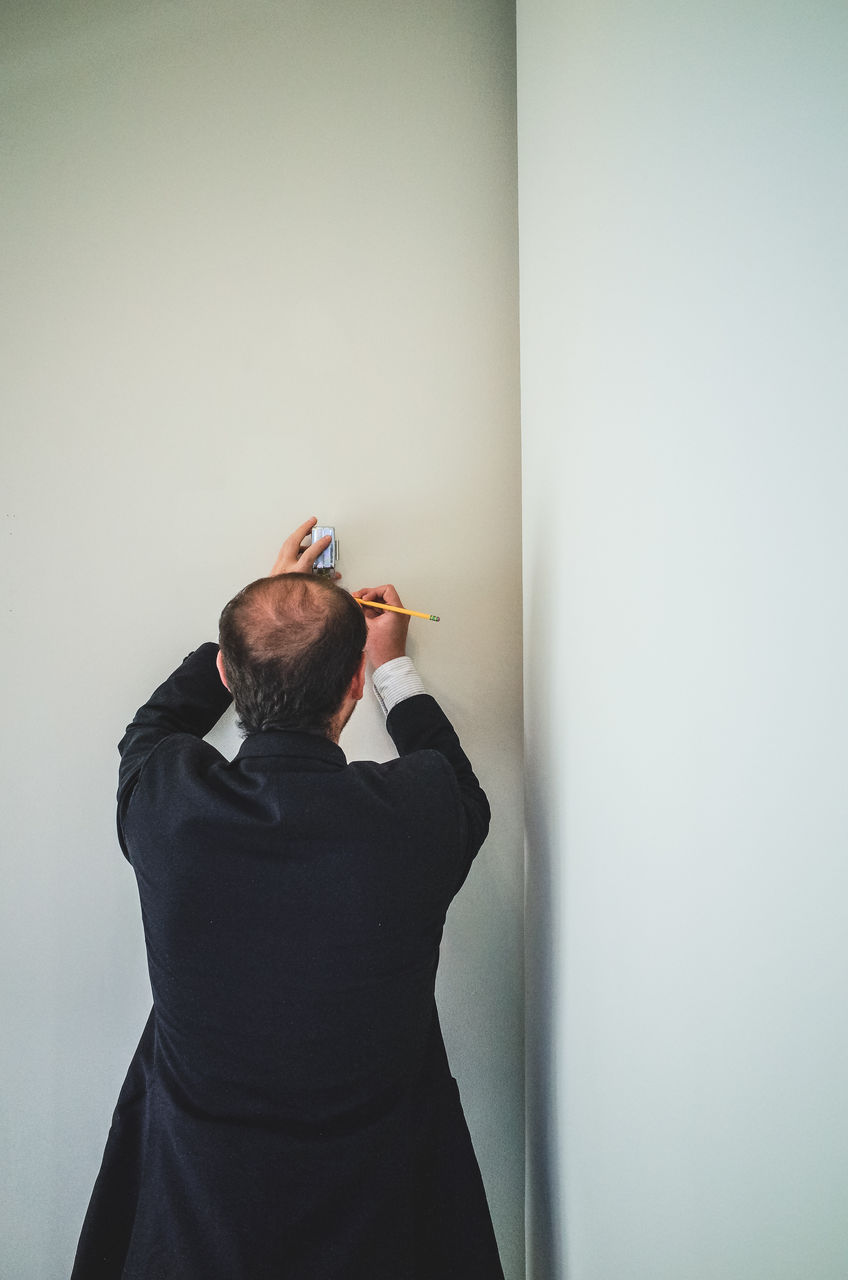 Rear view of man holding tape measure and marking on wall