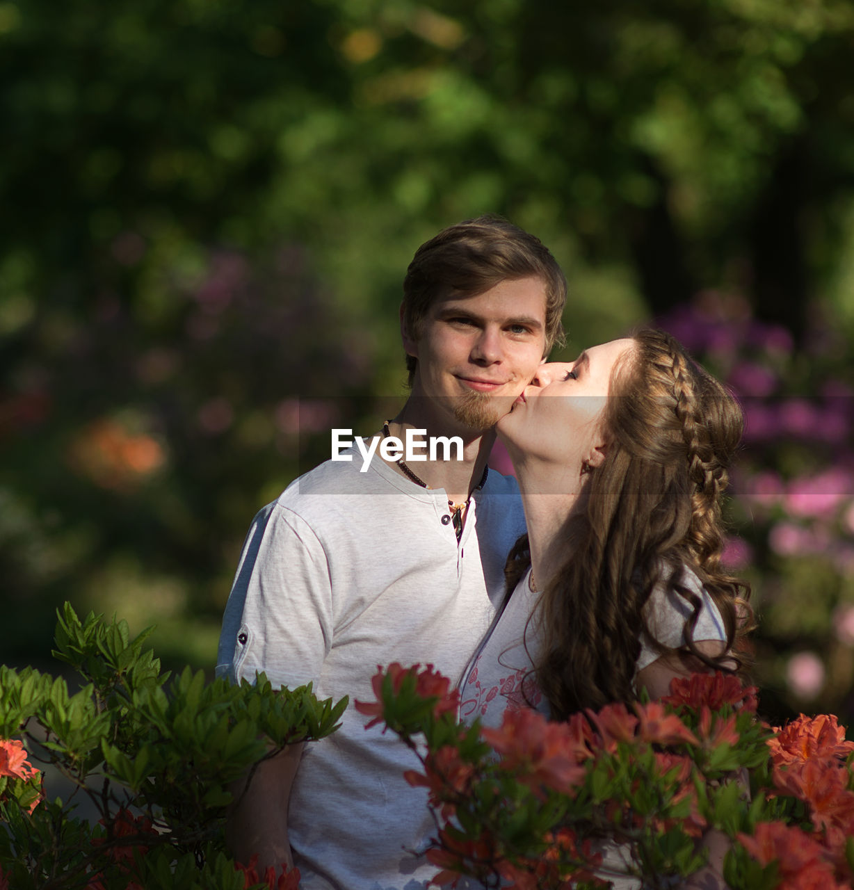 Woman kissing boyfriend standing amidst flowers at park