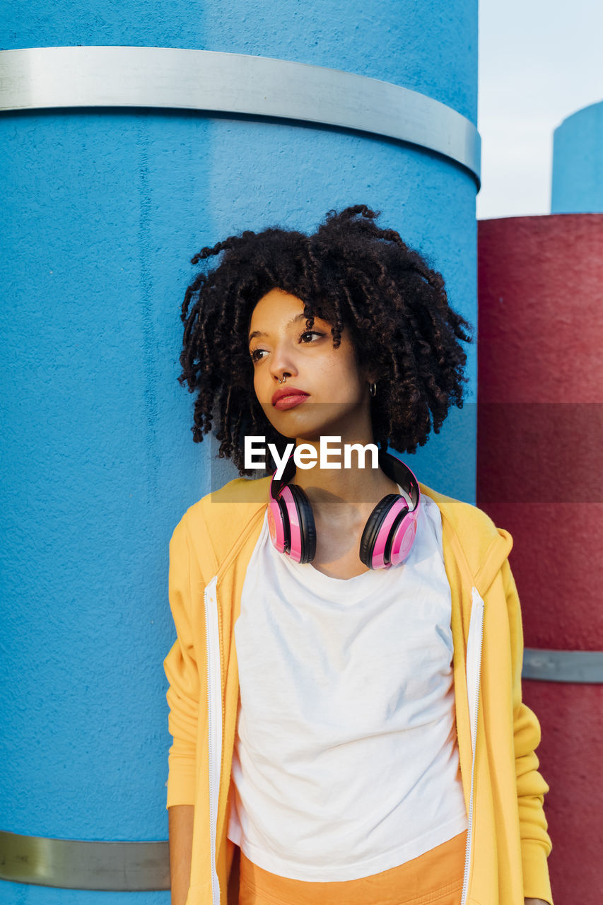 Young woman with curly hair in front of blue pipe