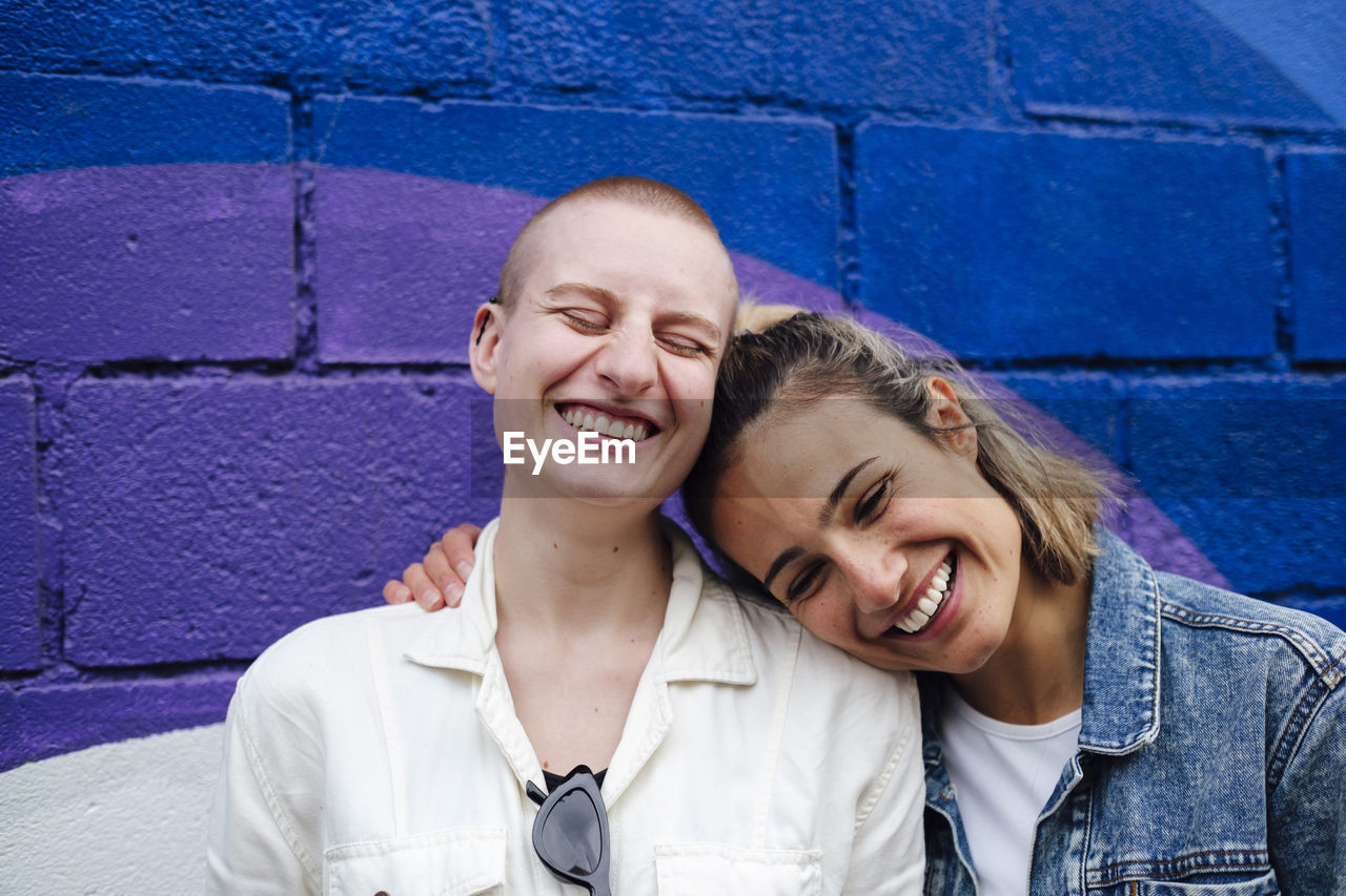 Cheerful lesbian couple having fun in front of wall