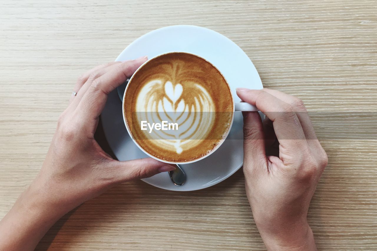 Directly above shot of hand holding coffee cup on table