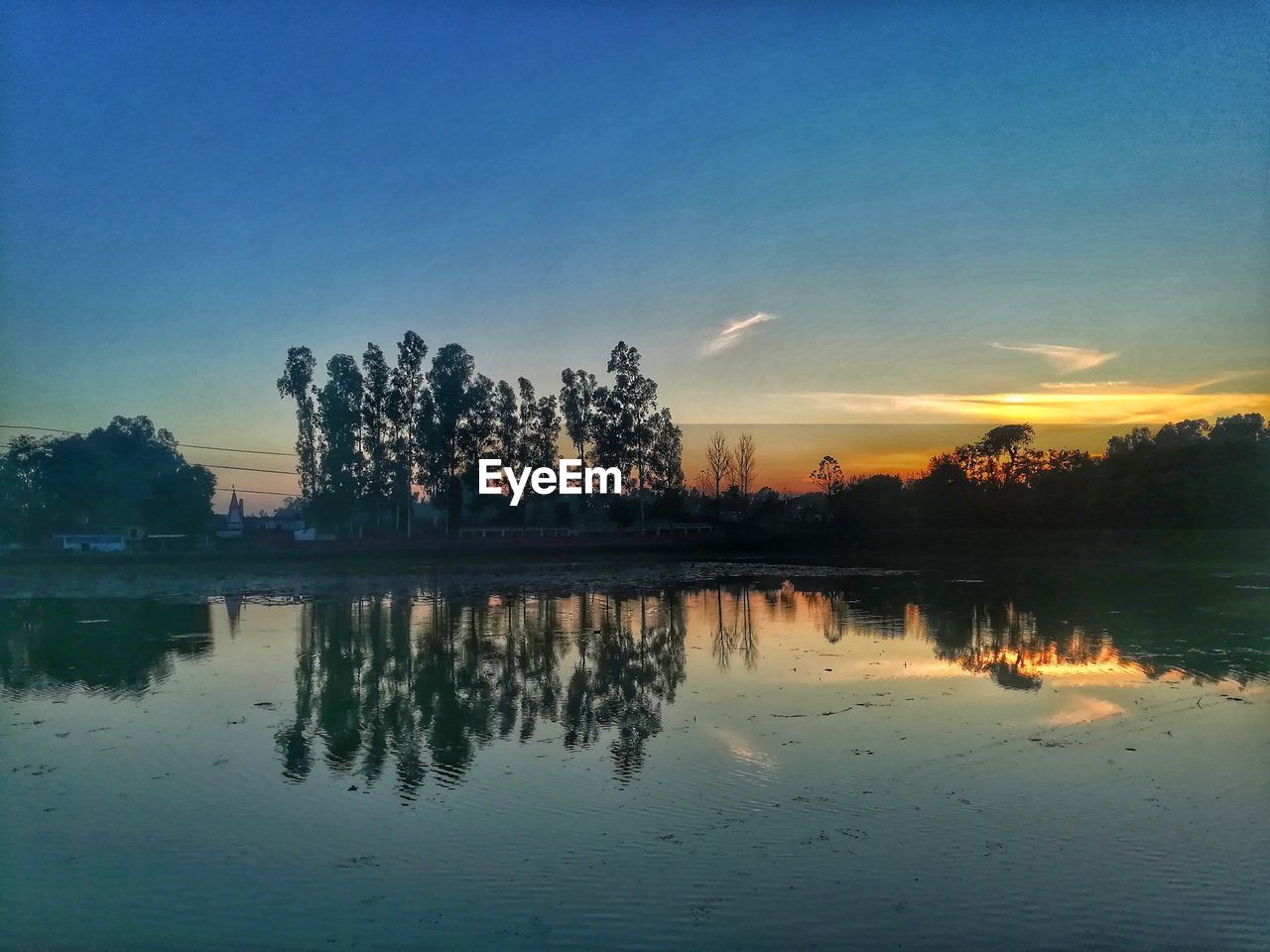 REFLECTION OF SILHOUETTE TREES IN LAKE AGAINST SKY DURING SUNSET