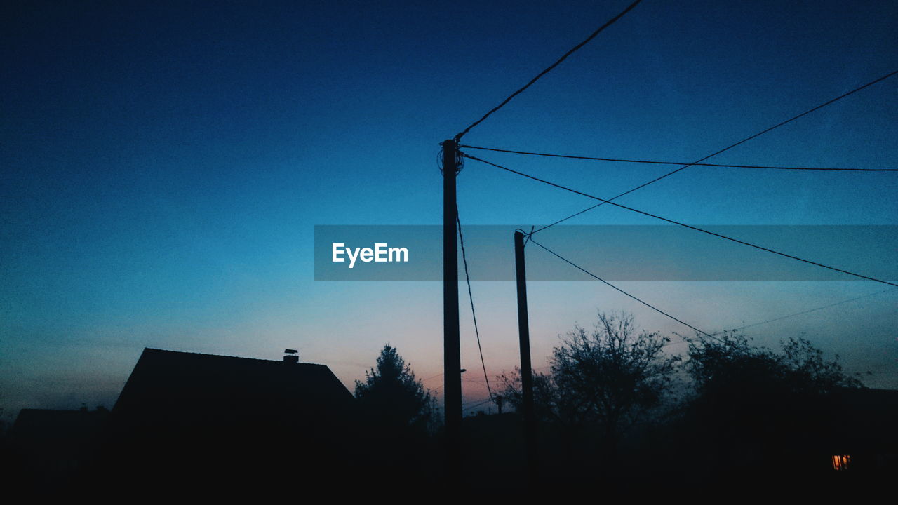 Low angle view of silhouette power lines against blue sky