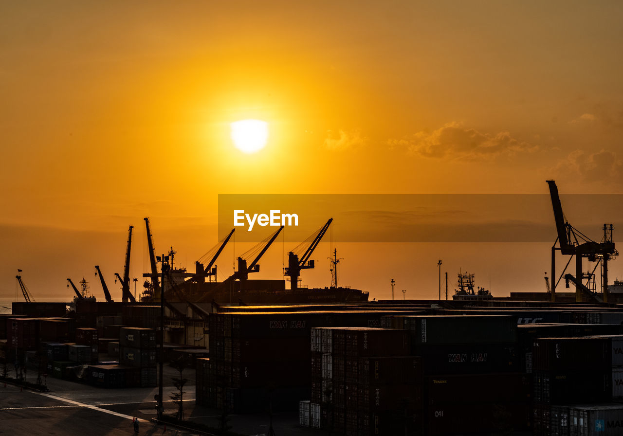 SILHOUETTE CRANES AT CONSTRUCTION SITE DURING SUNSET