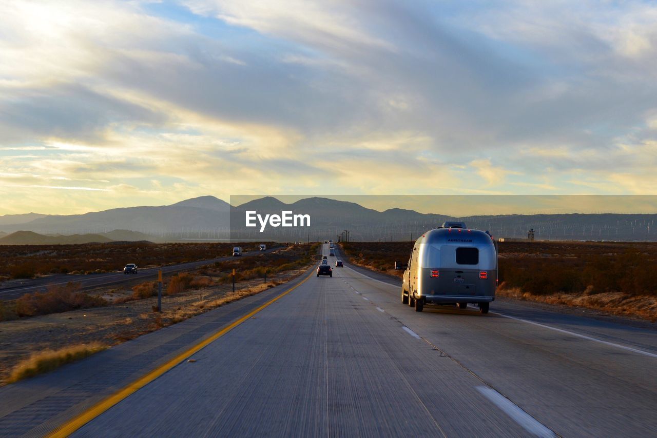 Vehicles on country road against cloudy sky