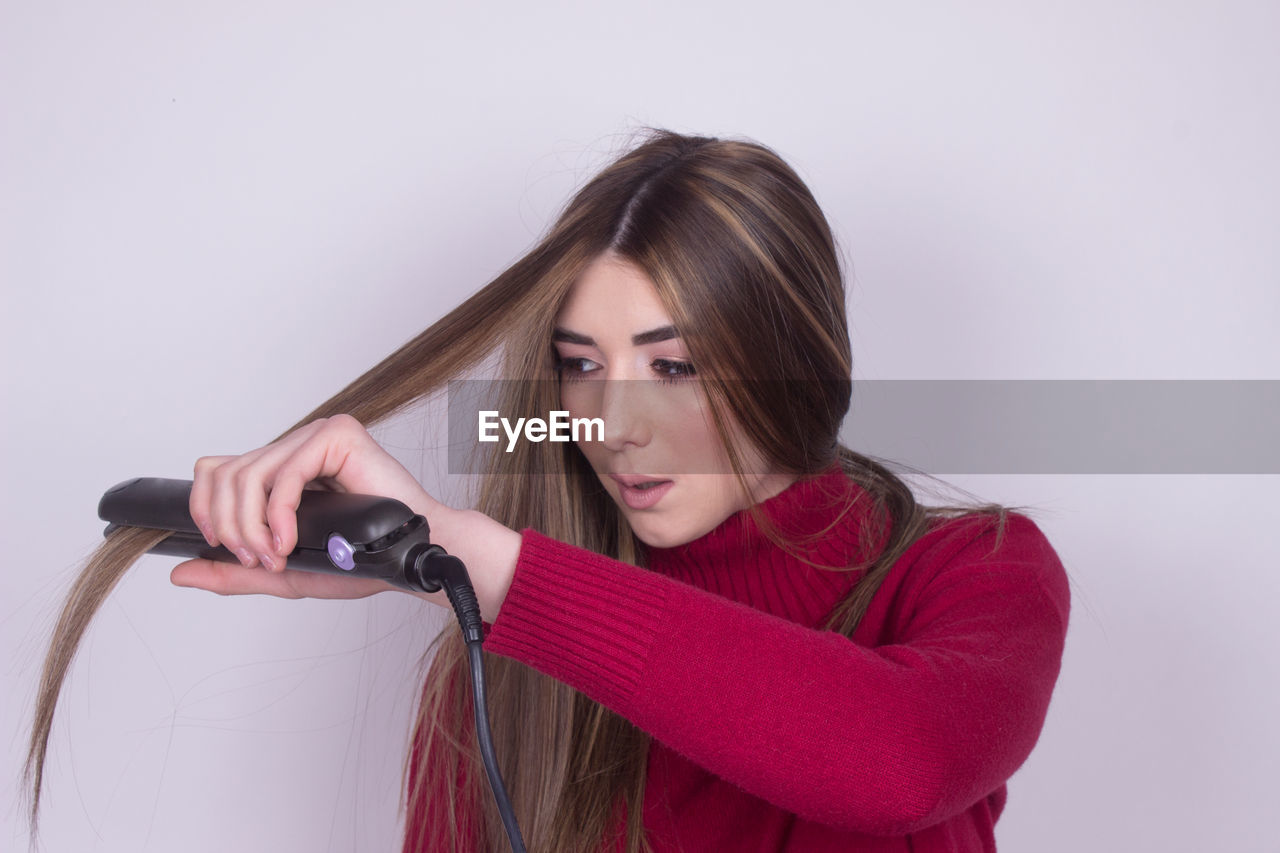 Beautiful young woman straightening her long hair against gray background