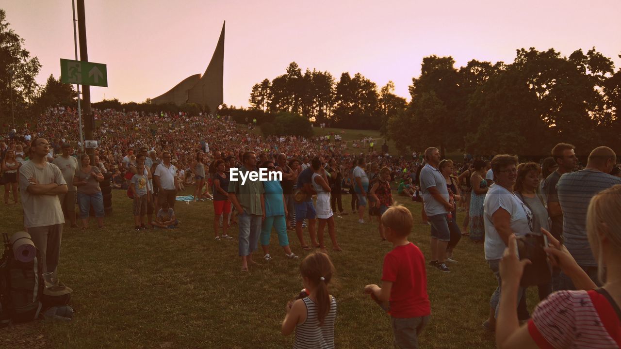 Crowd in park against sky during sunset