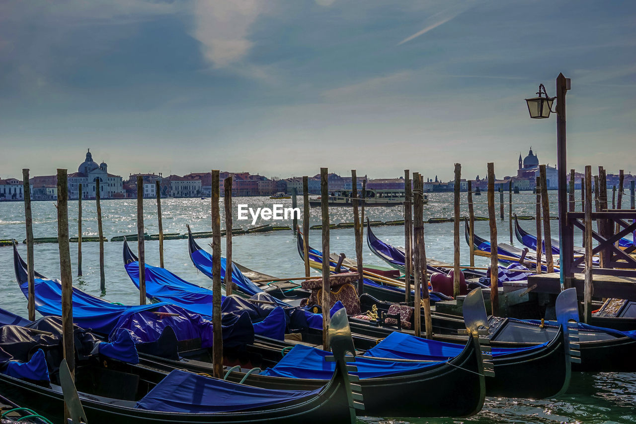 Boats moored in canal against cloudy sky