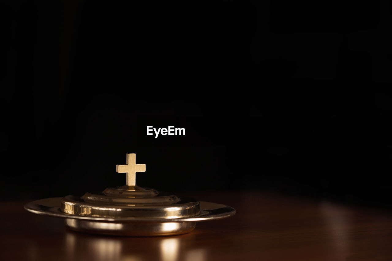 Close-up of cross on metal at table against black background