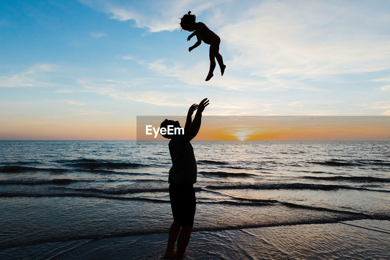 Father throws his daughter into the air at sunset on beach vacation