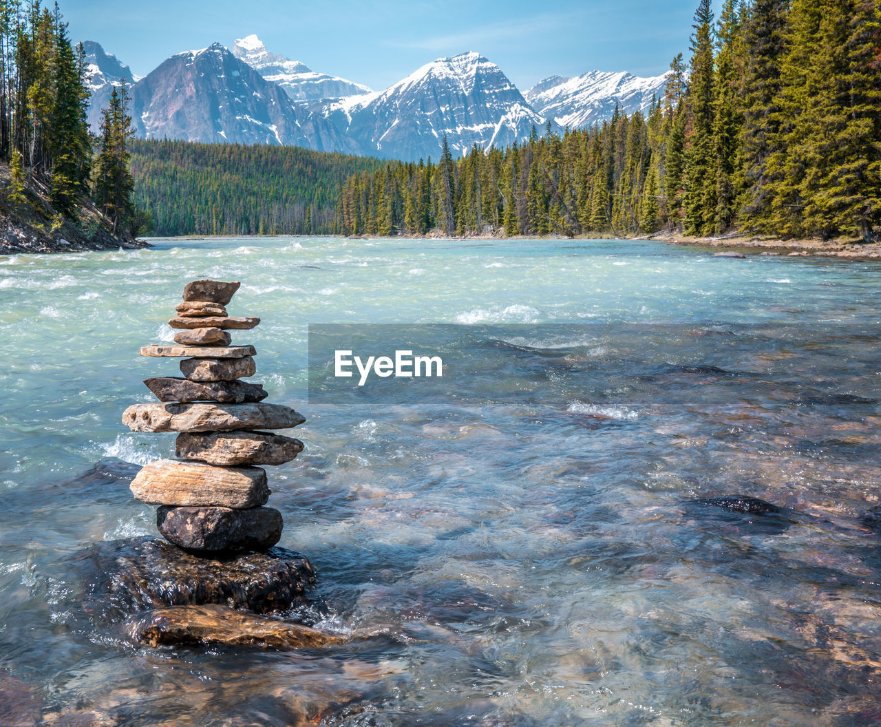 STACK OF ROCKS BY LAKE AGAINST MOUNTAIN