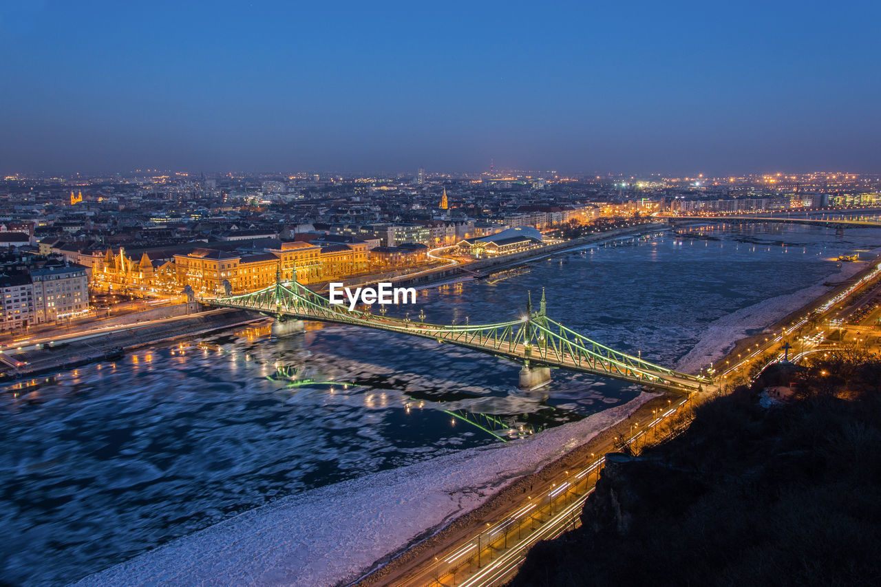 Aerial view of bridge over river with cityscape in background at night