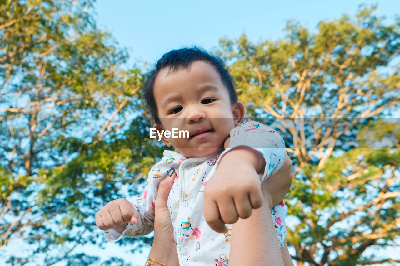 Cropped hand of mother holding son mid-air against tree