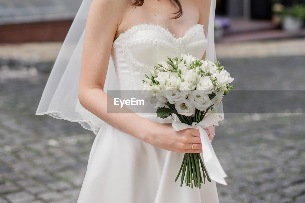 midsection of bride with bouquet