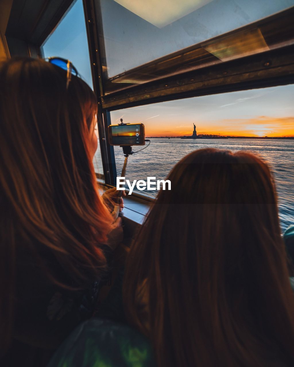 Rear view of women in ferry boat while looking at statue of liberty