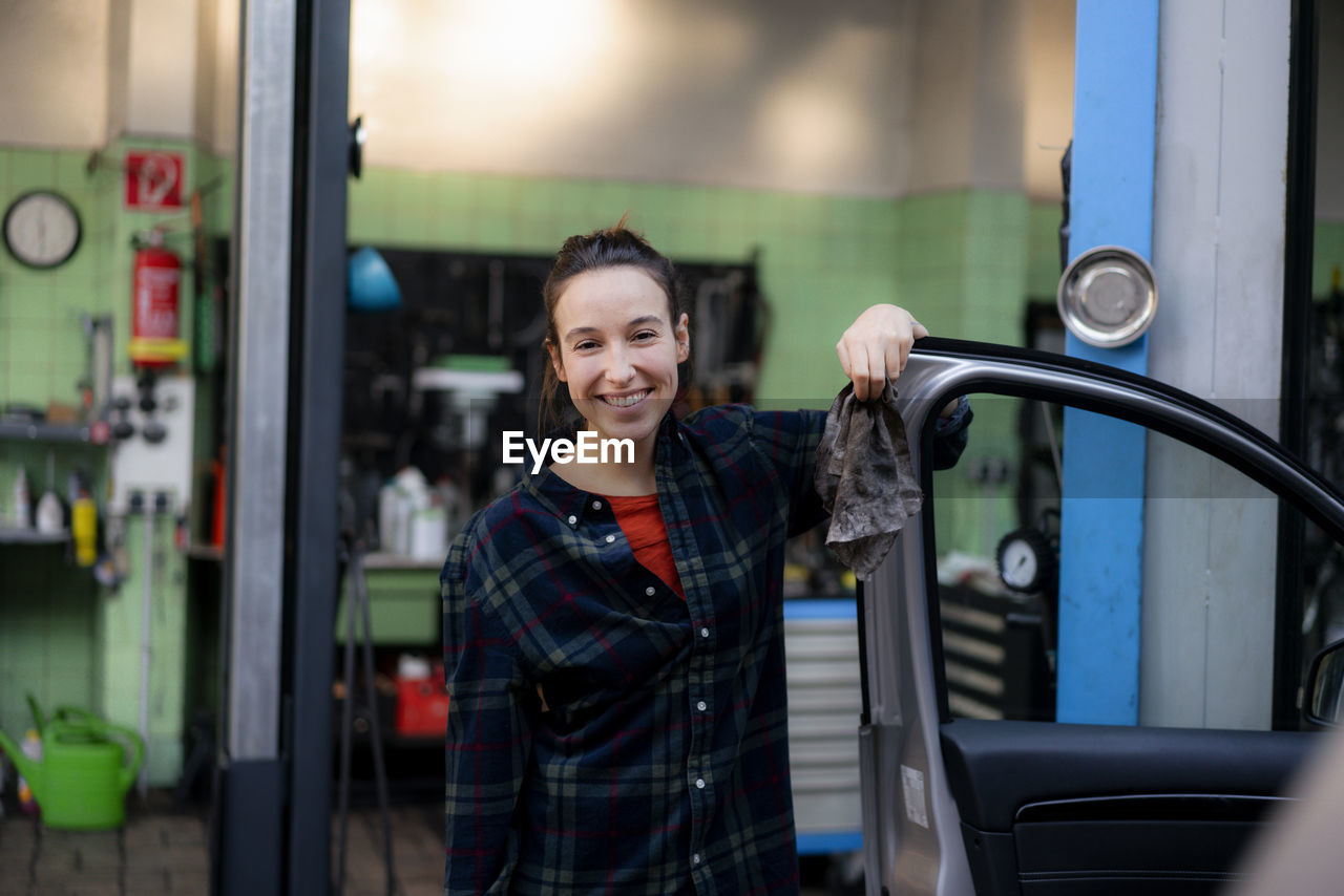 Smiling female mechanic opening car door at workshop