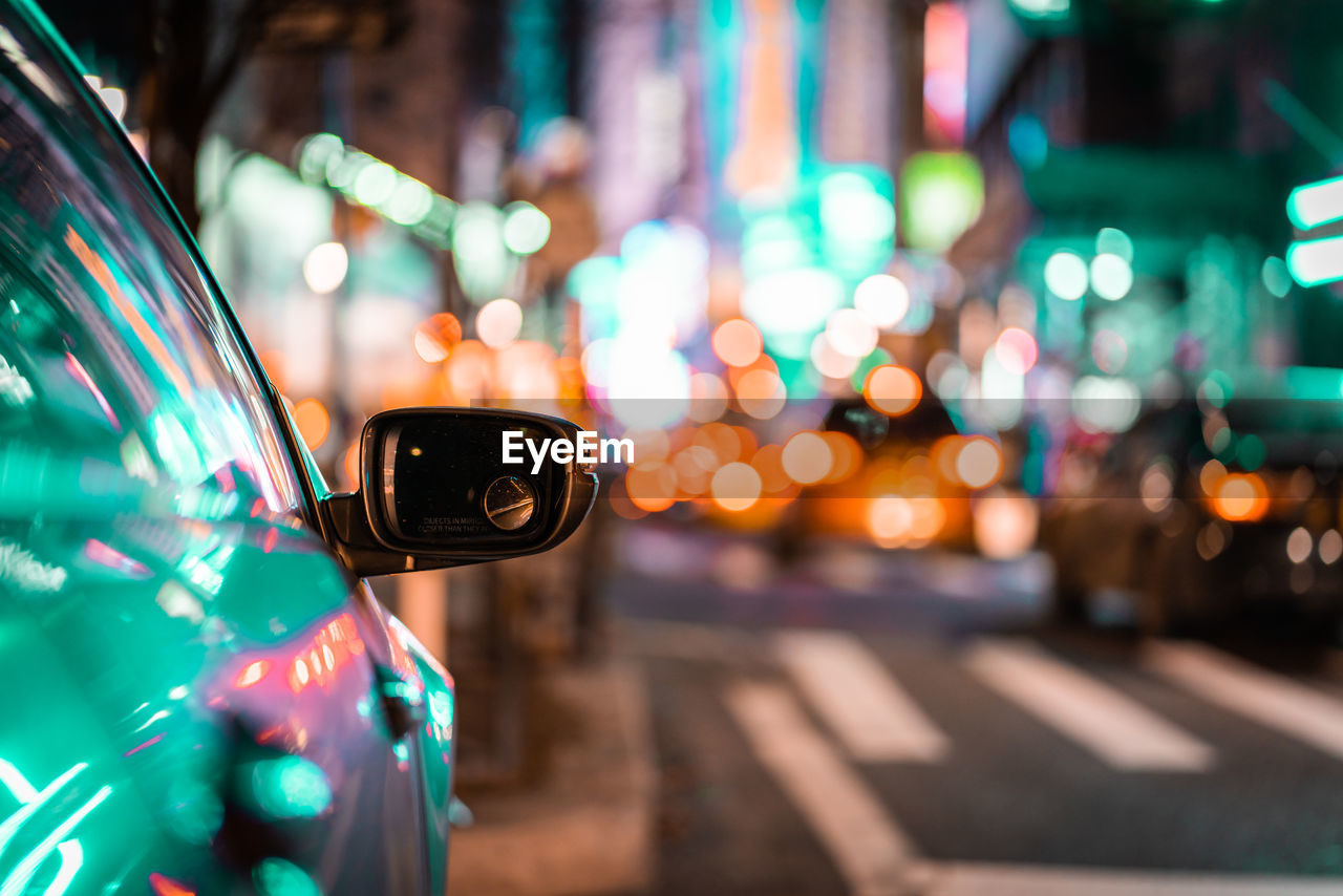 Close-up of car moving on road against illuminated lights at night