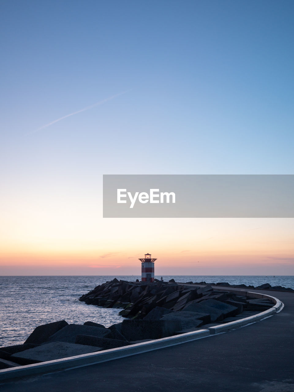 Lighthouse by sea against clear sky during sunset