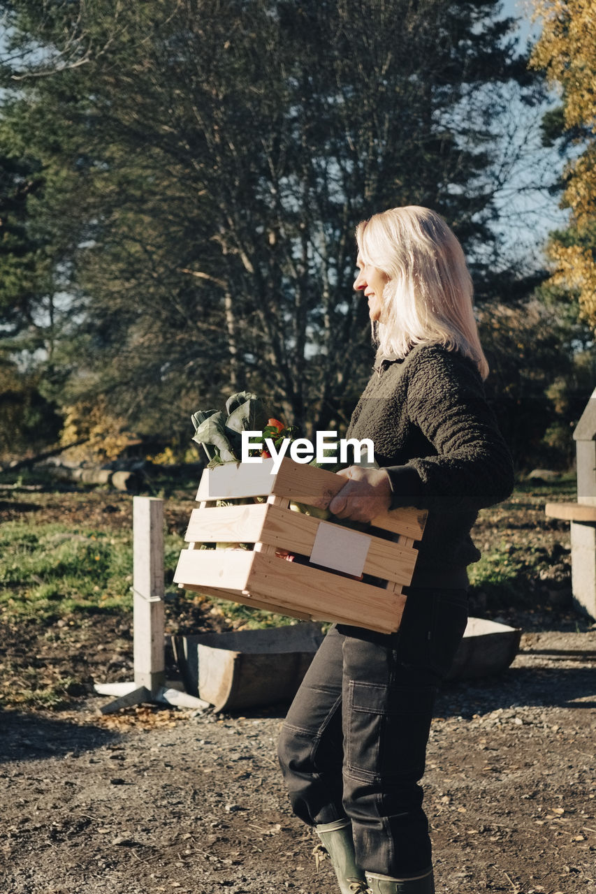 Side view of mature woman carrying crate full of vegetables at farmer's market