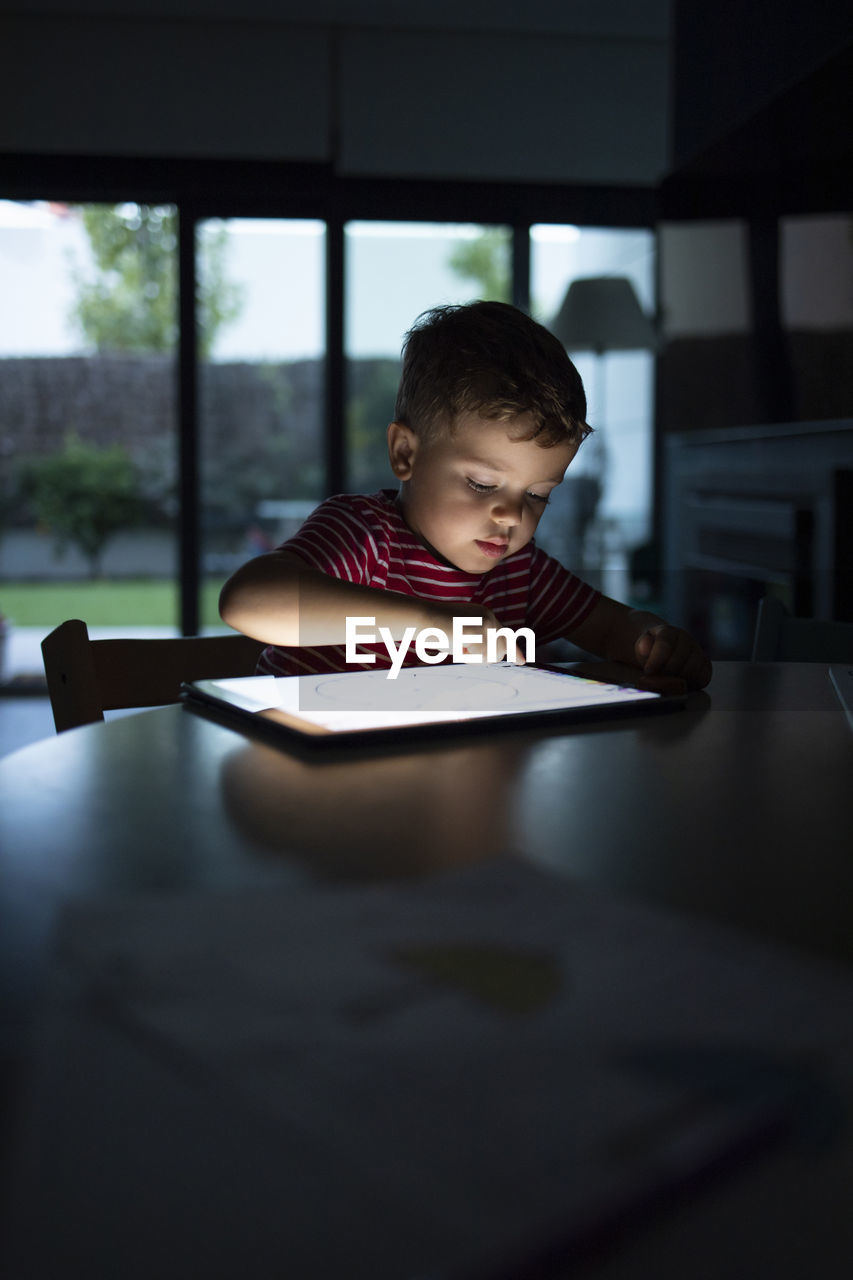 Boy using digital tablet while sitting at table in home