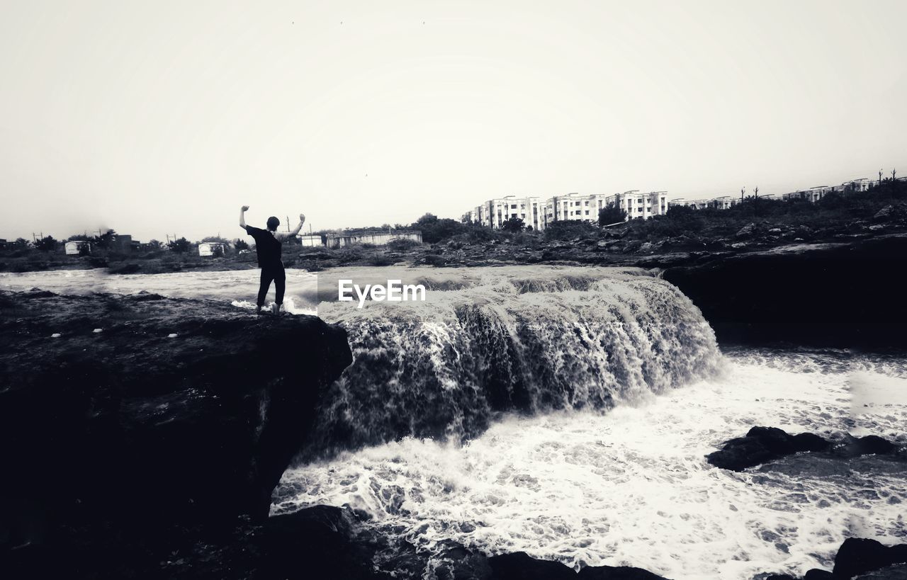 SILHOUETTE MAN STANDING ON ROCK AGAINST SEA