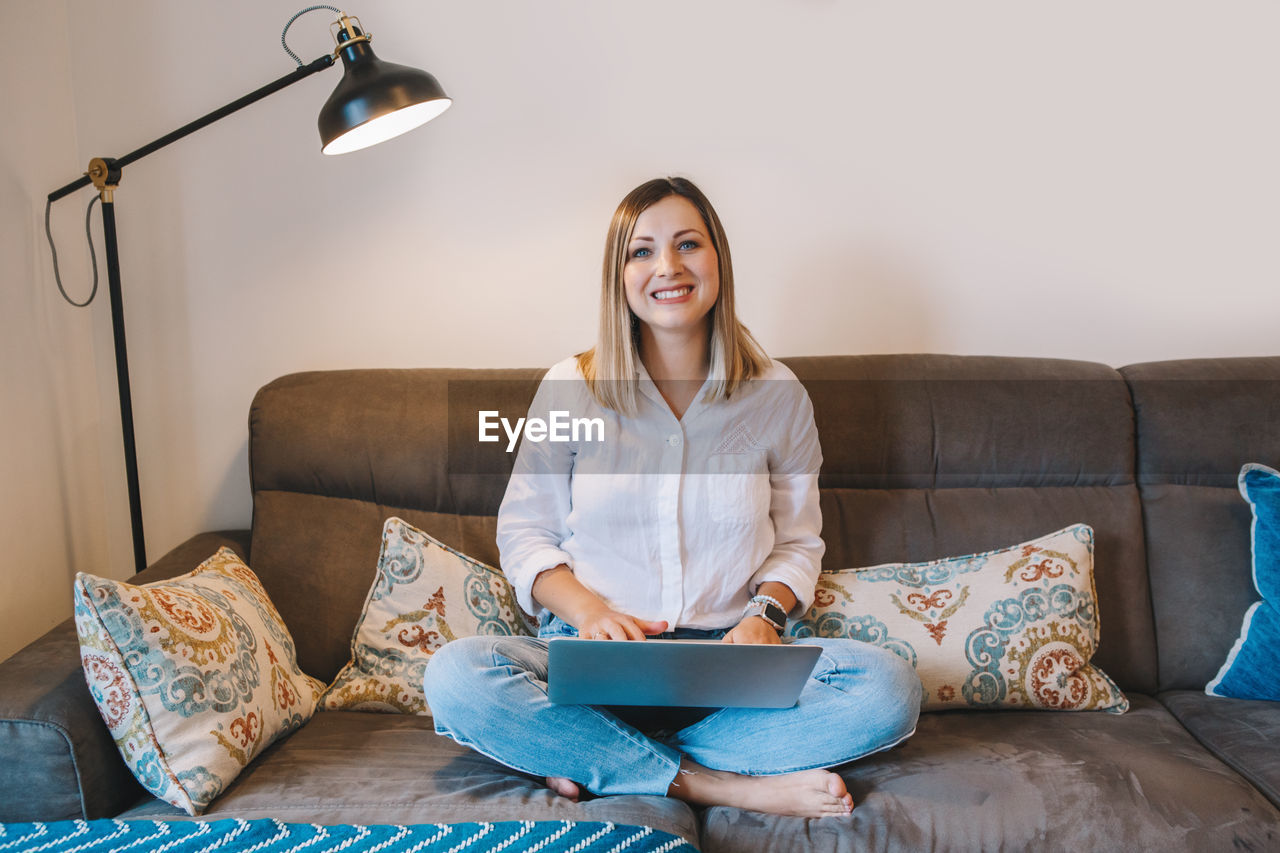 Woman sitting on couch in living room with laptop surfing internet. distant remote work from home. 