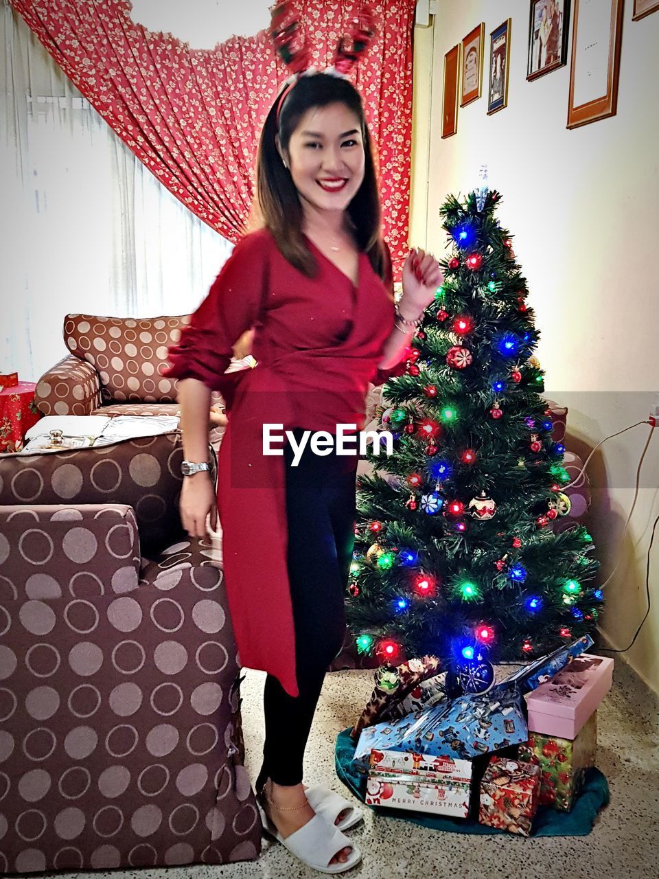 PORTRAIT OF YOUNG WOMAN AT CHRISTMAS TREE AT HOME