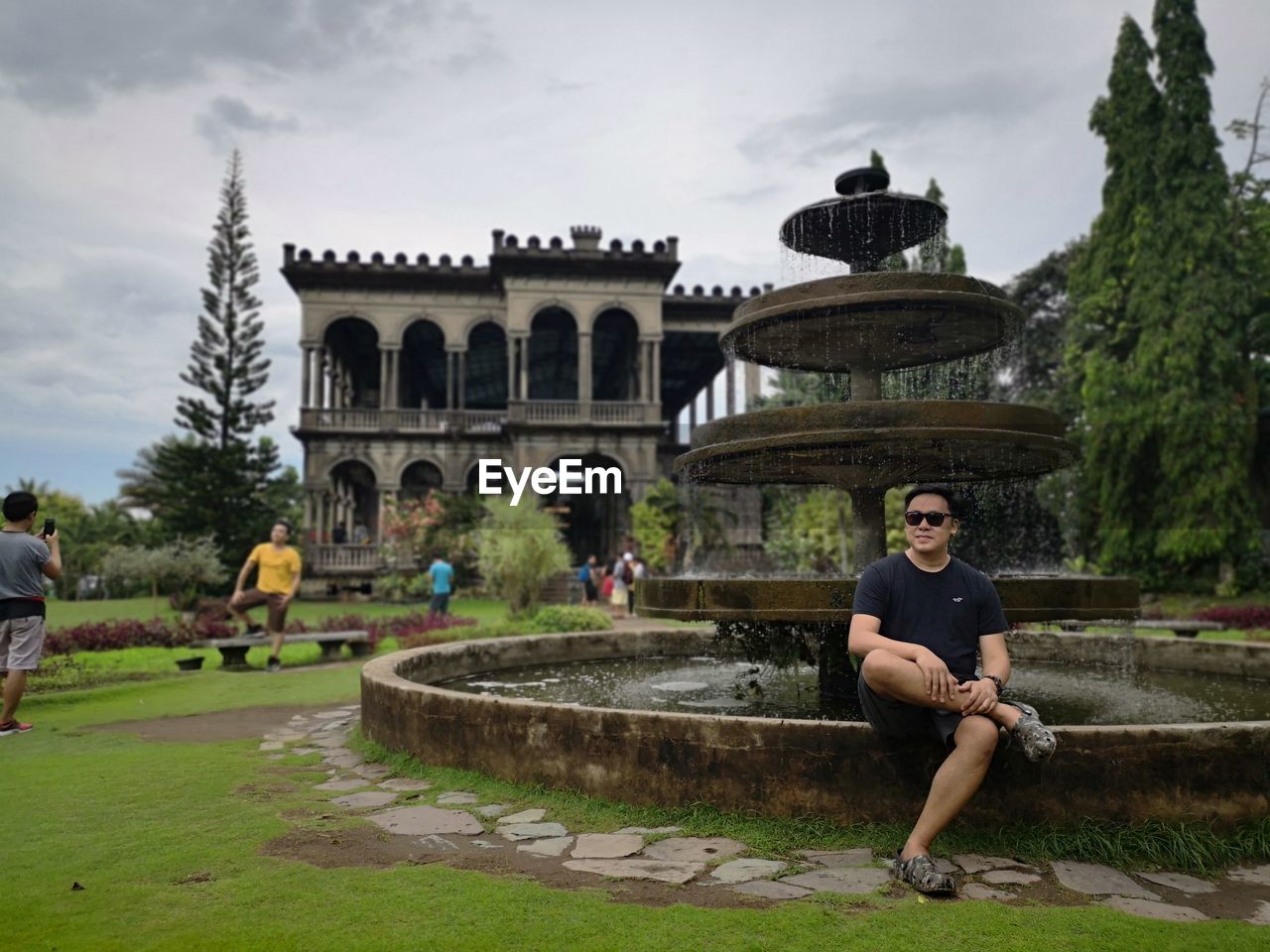 Full length of man sitting against fountain and sky