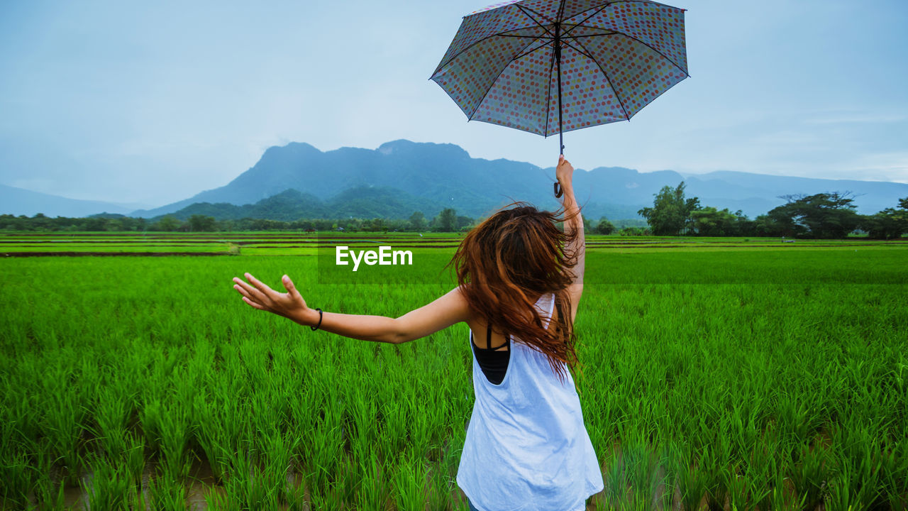 Rear view of woman with umbrella standing on field