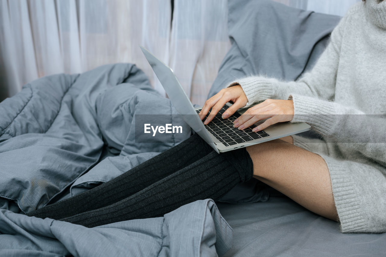 midsection of woman using laptop on bed